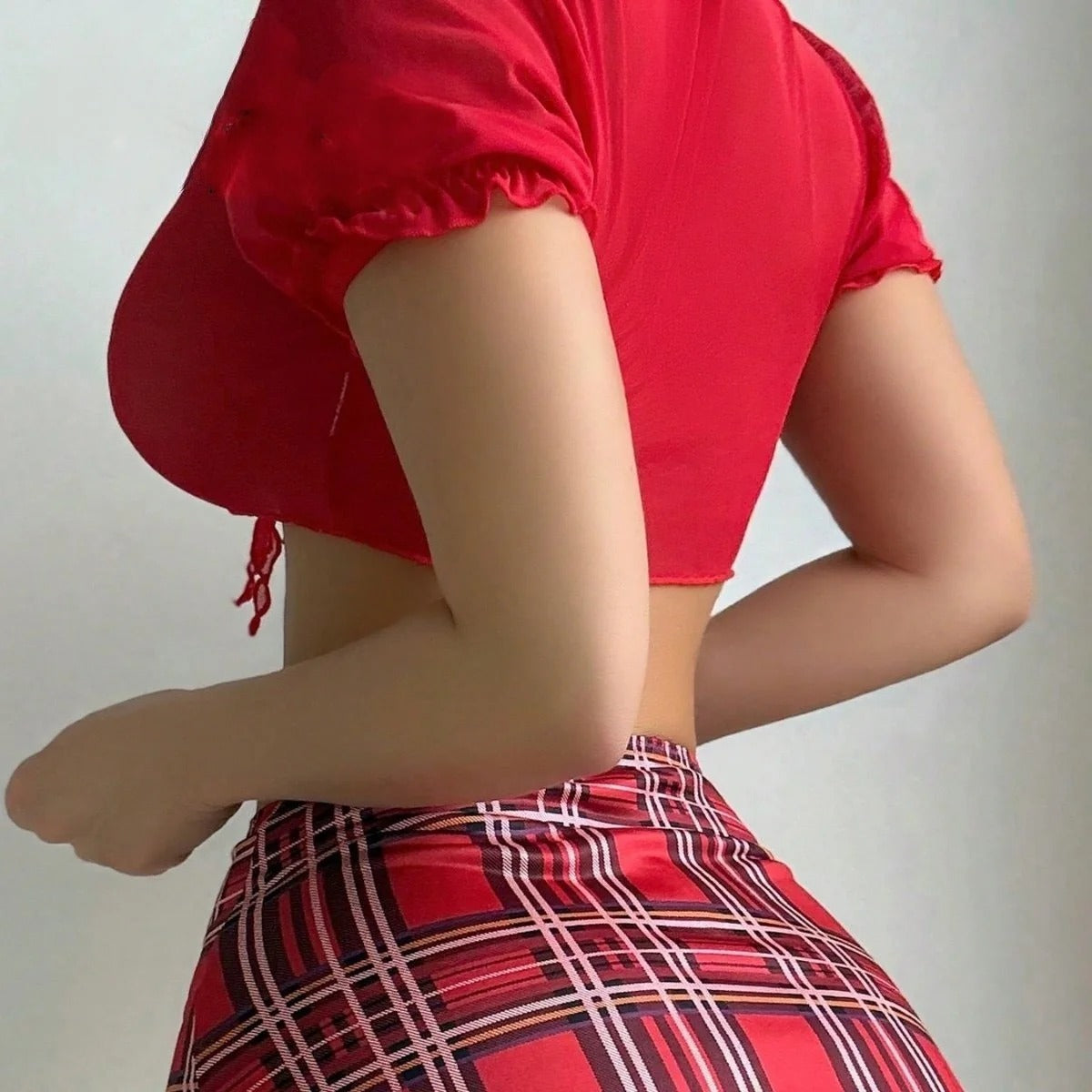 Person wearing a red top and plaid skirt against a plain background