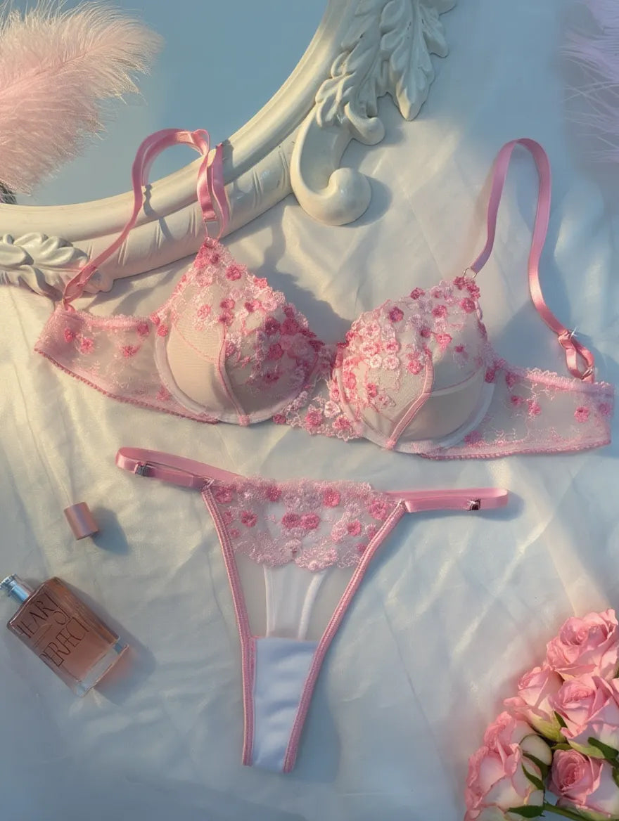 Pink floral lingerie set on a decorative surface with flowers and a mirror.